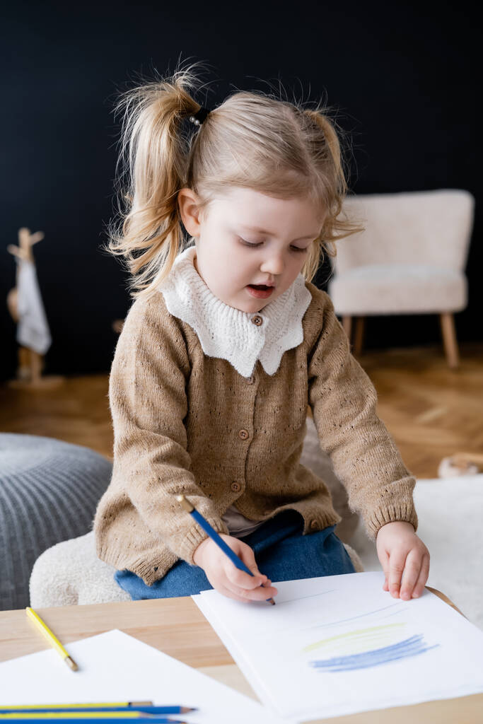 Tyttö piirustus sininen ja keltainen kyniä istuessaan kotona - Valokuva, kuva