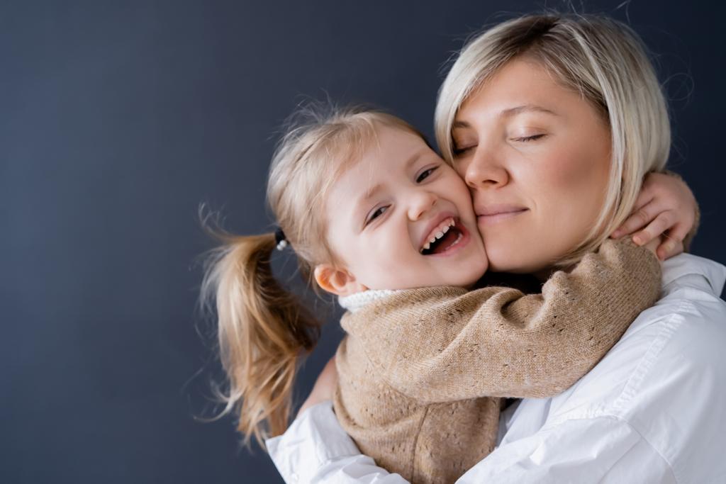 laughing girl embracing mother while looking at camera isolated on black - Photo, Image