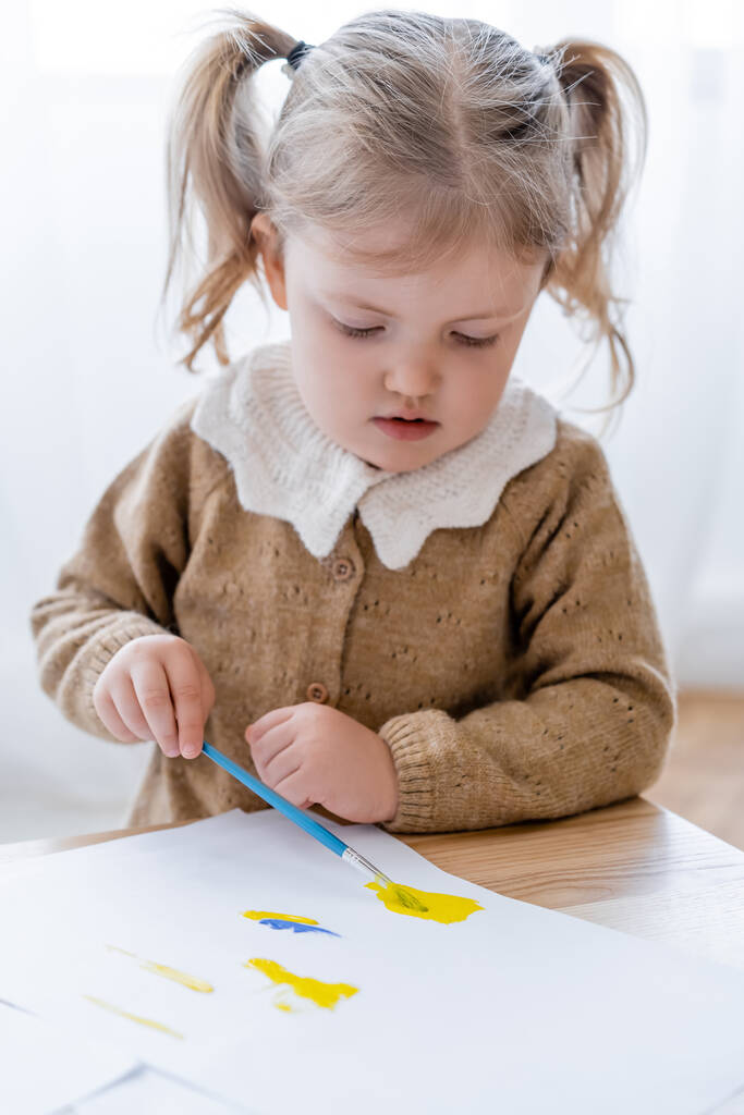 niña con coletas dibujando con pinturas azules y amarillas en casa - Foto, Imagen