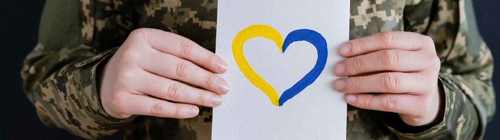 levágott kilátás katonai nő gazdaság fehér kártya kék és sárga szív elszigetelt fekete, banner - Fotó, kép