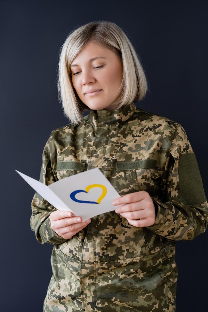 mulher em cartão postal de leitura uniforme militar com coração azul e amarelo isolado em preto - Foto, Imagem