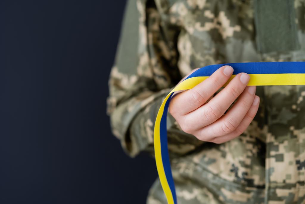 частковий вигляд жінки у військовій формі, що тримає синьо-жовту стрічку ізольовано на чорному
 - Фото, зображення