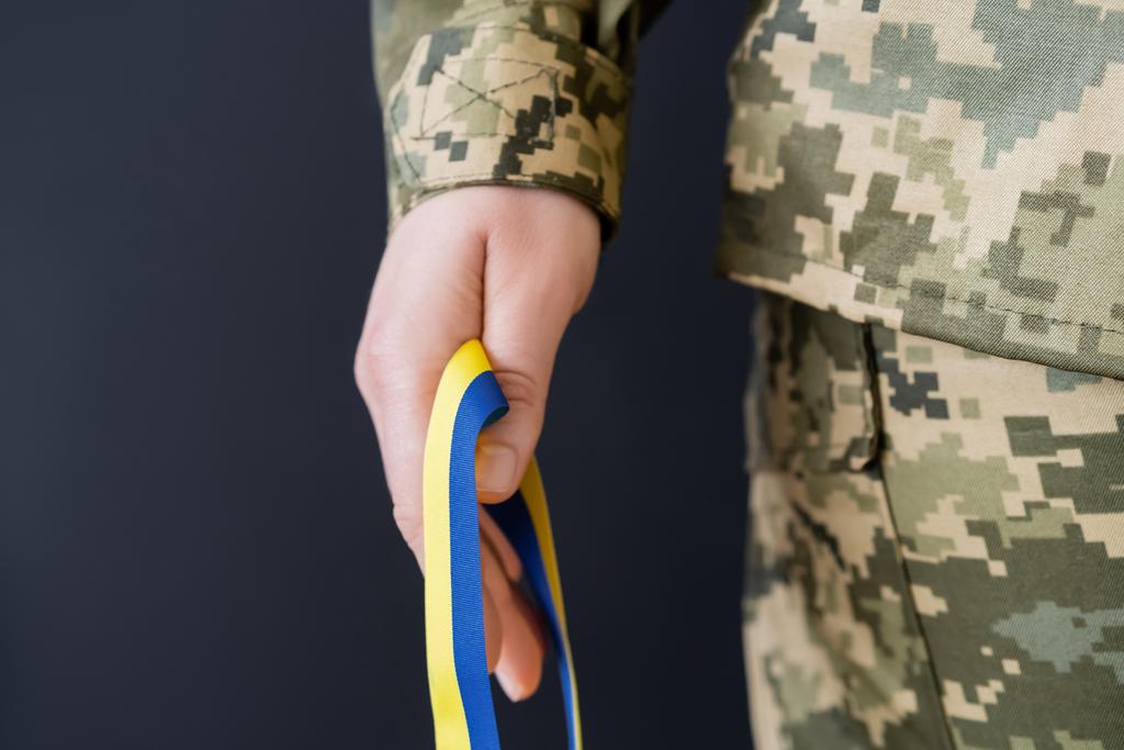partial view of military woman holding blue and yellow ribbon isolated on black - Photo, Image