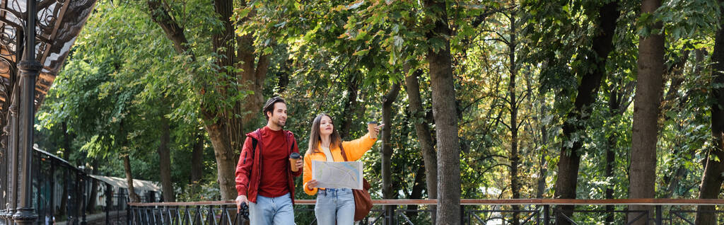 Traveler holding takeaway drink and binoculars near girlfriend con mappa sulla strada urbana, banner  - Foto, immagini