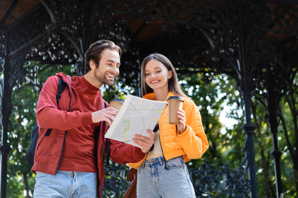 Positives Touristenpaar mit Karte und Coffee to go  - Foto, Bild