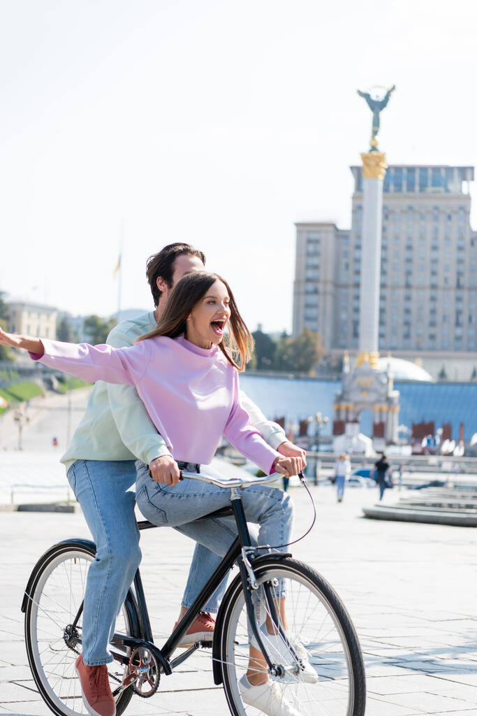 KYIV, UCRANIA - 1 de septiembre de 2021: Emocionada mujer montando en bicicleta con su novio en la Plaza de la Independencia - Foto, imagen