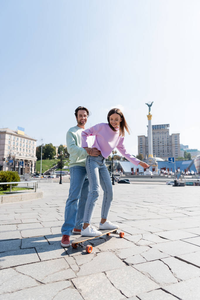 KYIV, UCRAINA - 1 SETTEMBRE 2021: Felice uomo che abbraccia la fidanzata cavalcando penny board sulla strada urbana di Kiev - Foto, immagini