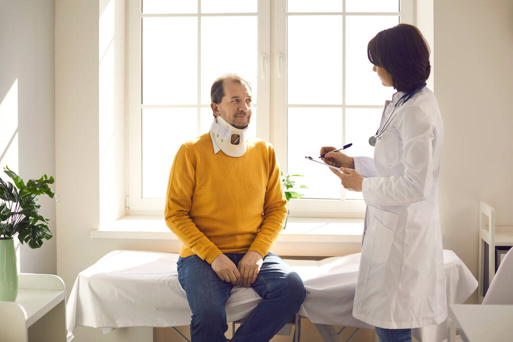 Paziente anziano con un collare cervicale che ascolta il suo medico in ospedale - Foto, immagini