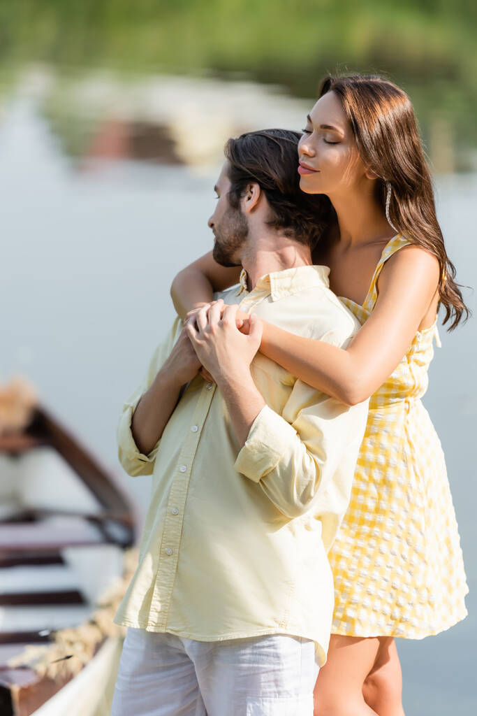 mujer joven en vestido abrazando novio barbudo cerca del lago - Foto, imagen
