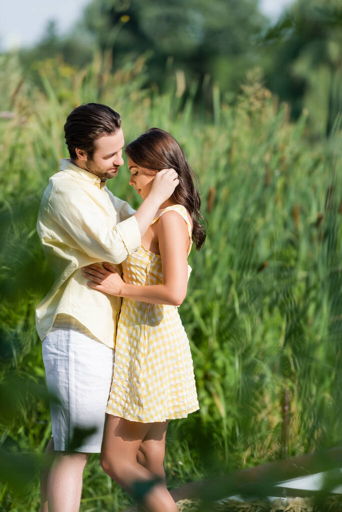 bearded man looking at young girlfriend in dress near lake - Photo, Image