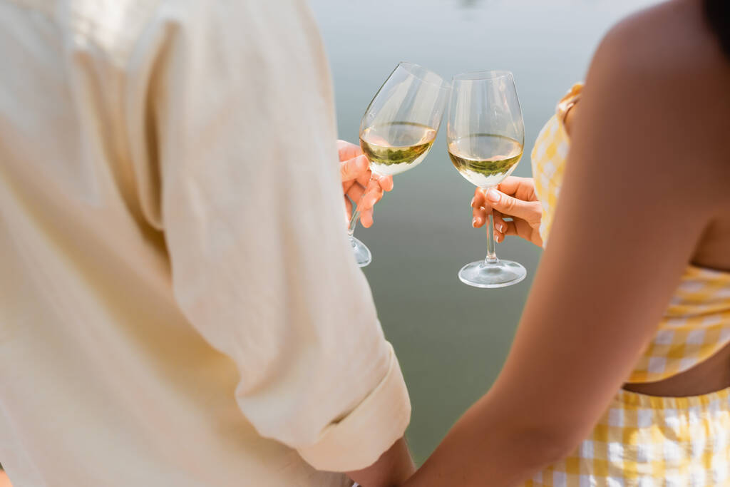 湖の近くでワインとロマンチックなカップルクリンクグラスのクロップドビュー - 写真・画像
