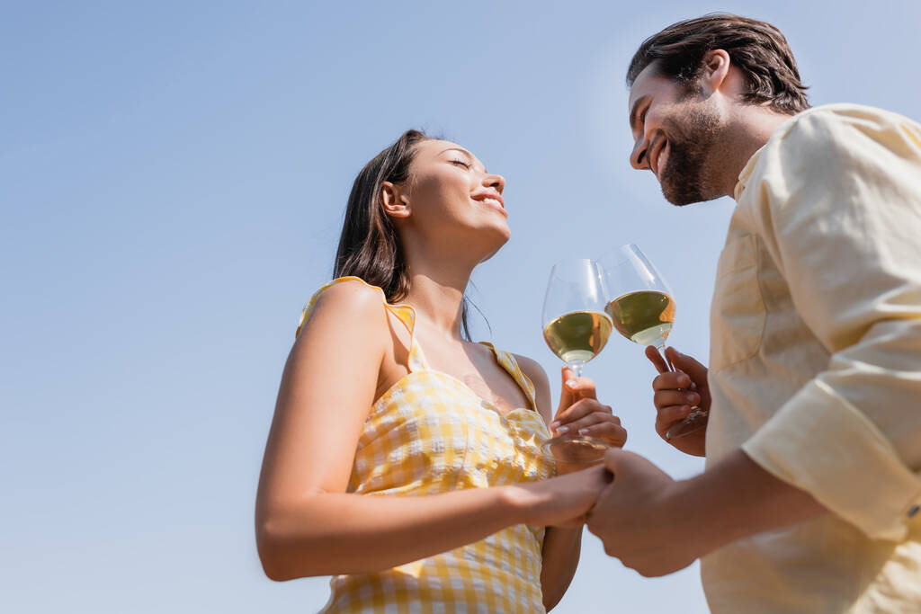 low angle view of young couple in summer clothes clinking glasses with wine  - Photo, Image