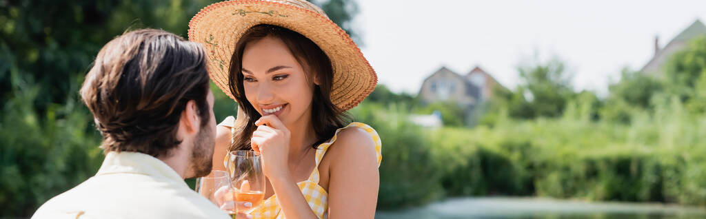 vzrušená žena v slamáku drží sklenici vína a dívá se na přítele, banner - Fotografie, Obrázek