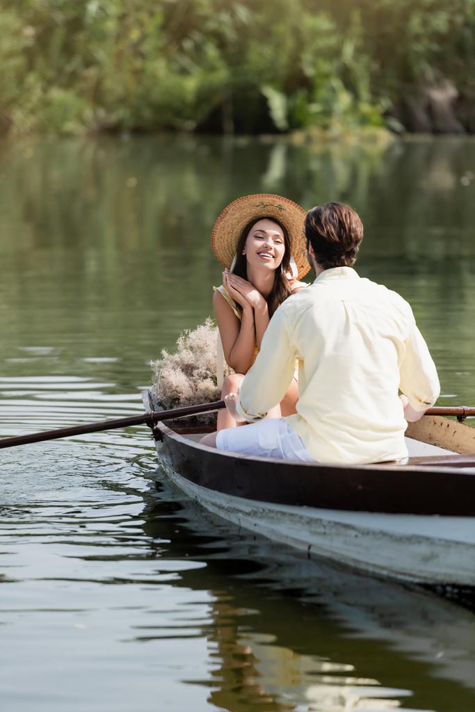 onnellinen nainen olkihattu katselee romanttinen poikaystävä aikana veneen ratsastaa - Valokuva, kuva