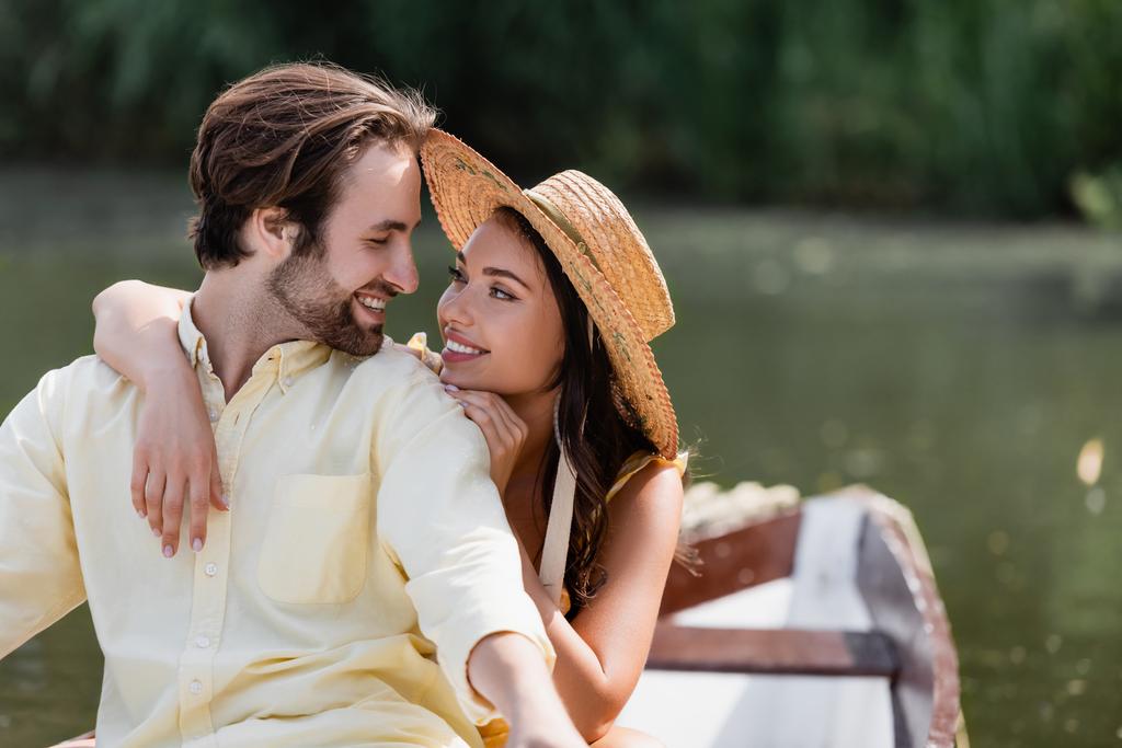 усміхнена молода жінка в солом'яному капелюсі обіймає щасливого чоловіка під час романтичної подорожі на човні
  - Фото, зображення