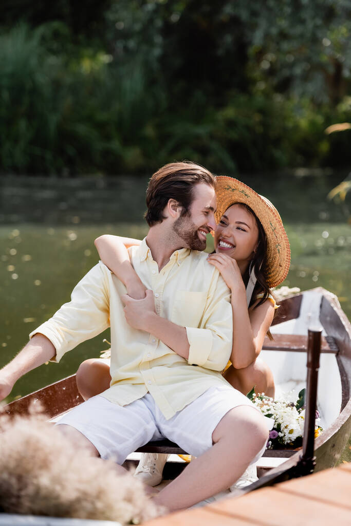 Hasır şapkalı mutlu genç kadın romantik tekne gezisinde gülümseyen adama sarılıyor.  - Fotoğraf, Görsel