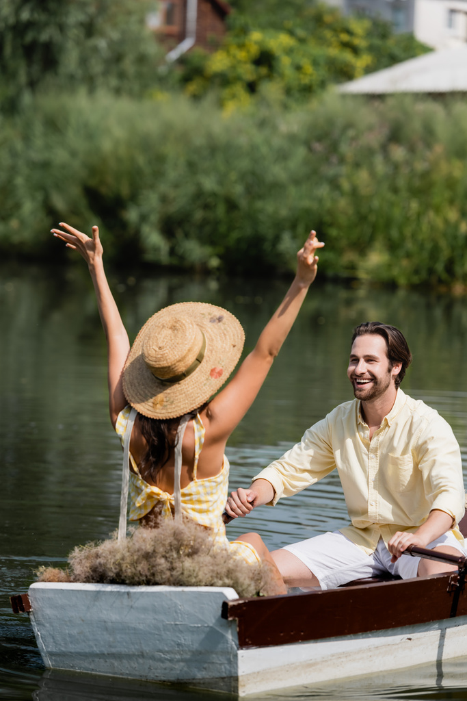 Mutlu sakallı bir adam hasır şapkalı kız arkadaşına bakıyor. Tekne gezintisi sırasında ellerini uzatmış.  - Fotoğraf, Görsel