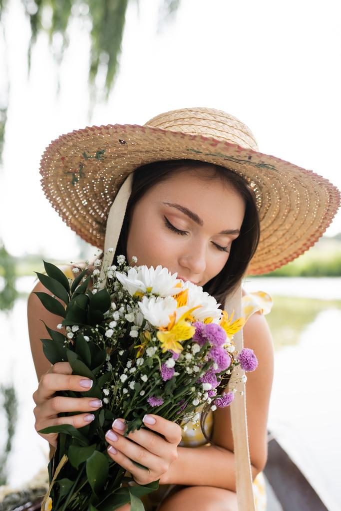 junge Frau mit Strohhut, die nach Blumen riecht  - Foto, Bild