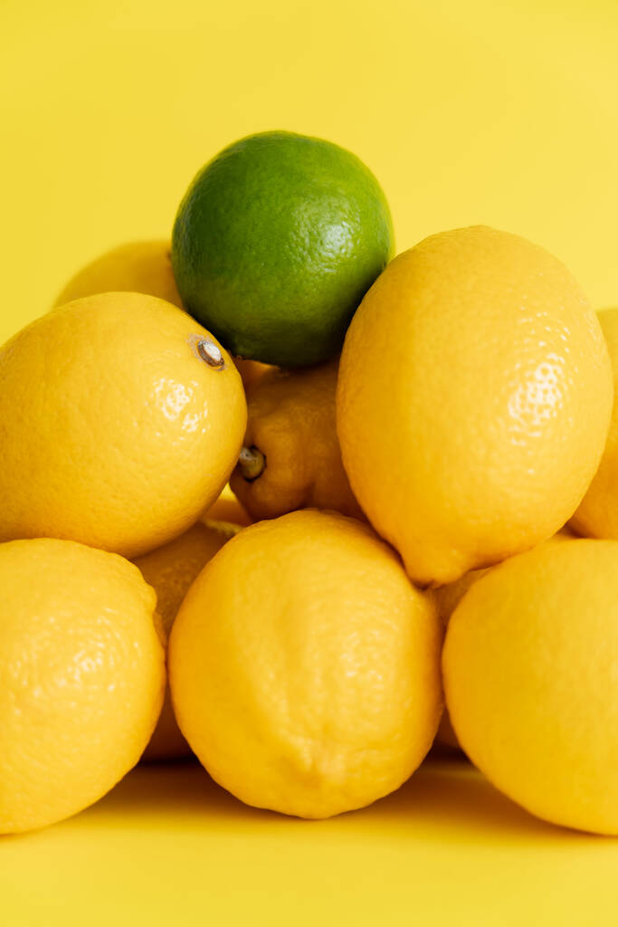 Nahaufnahme von grünen Limetten auf Zitronen auf gelber Oberfläche  - Foto, Bild