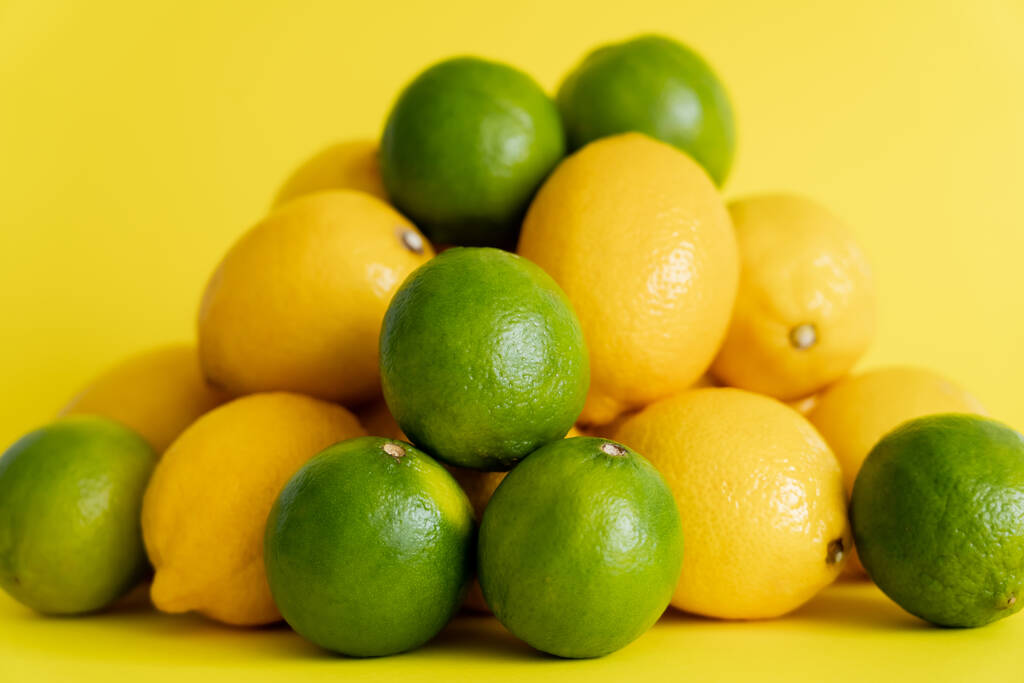 Juicy limes near heap of blurred lemons on yellow surface  - Foto, Bild