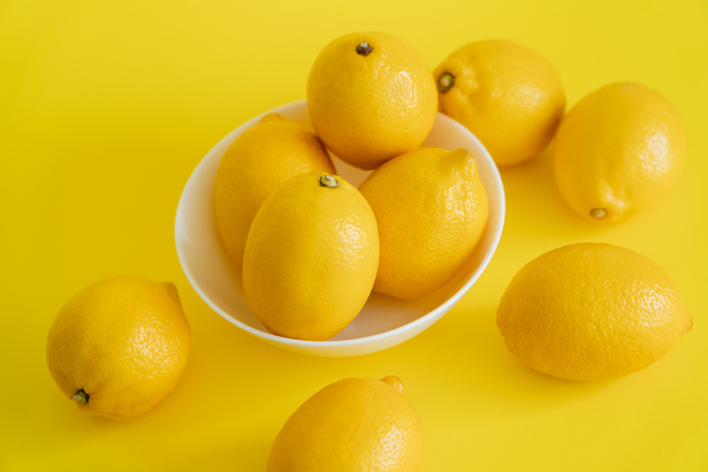 High angle view of ripe lemons in bowl on yellow surface  - Photo, image