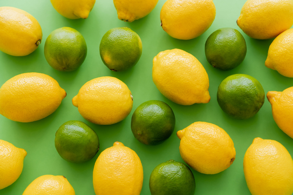 Vlakke lay-out van citroenen en limoenen op groene achtergrond - Foto, afbeelding