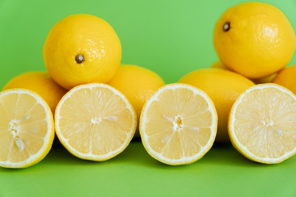 Φωτεινά μισά και ολόκληρα λεμόνια σε πράσινο φόντο  - Φωτογραφία, εικόνα