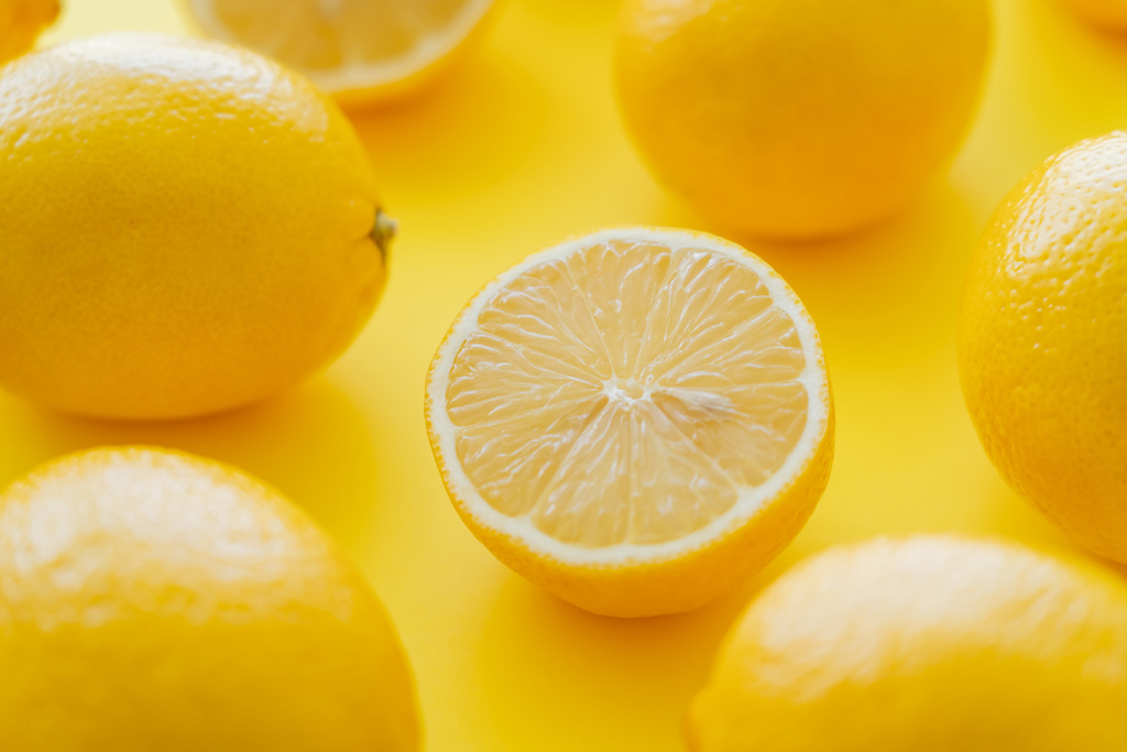 Vista ravvicinata di limoni interi tagliati e sfocati sulla superficie gialla  - Foto, immagini
