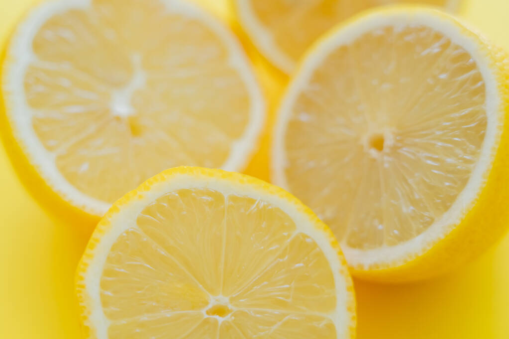 Close up view of blurred halves of lemons on yellow surface  - Foto, Imagen