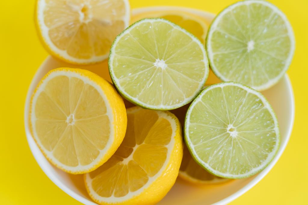 Widok z góry świeże cytryny i limonki w misce na żółtym tle - Zdjęcie, obraz