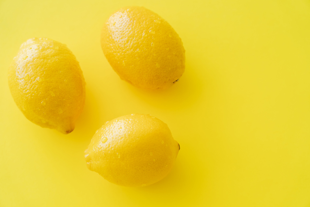 Bovenaanzicht van rijpe citroenen met natte schil op geel oppervlak - Foto, afbeelding
