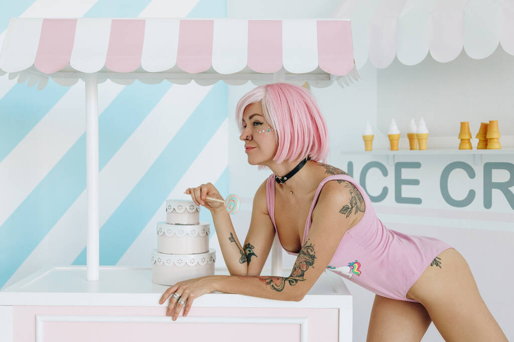 Szexi fiatal tetovált nő rózsaszín frizura és gyönyörű smink gazdaság édes színes nyalóka cukorka - Fotó, kép