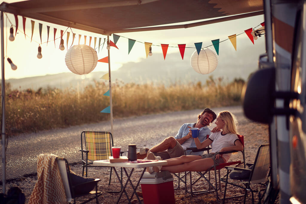 Junges Paar sitzt vor Wohnmobil und trinkt .Reise- und Freundschaftsfeier - Foto, Bild