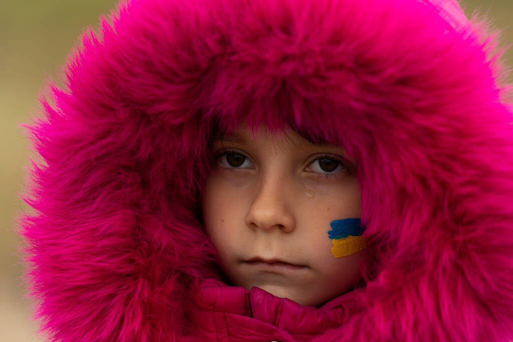 Una niña refugiada ucraniana con una bandera ucraniana pintada en su mejilla está triste por su hogar perdido. Detener la guerra en Ucrania. Ayuda a salvar a la nación ucraniana. Foto de alta calidad - Foto, Imagen