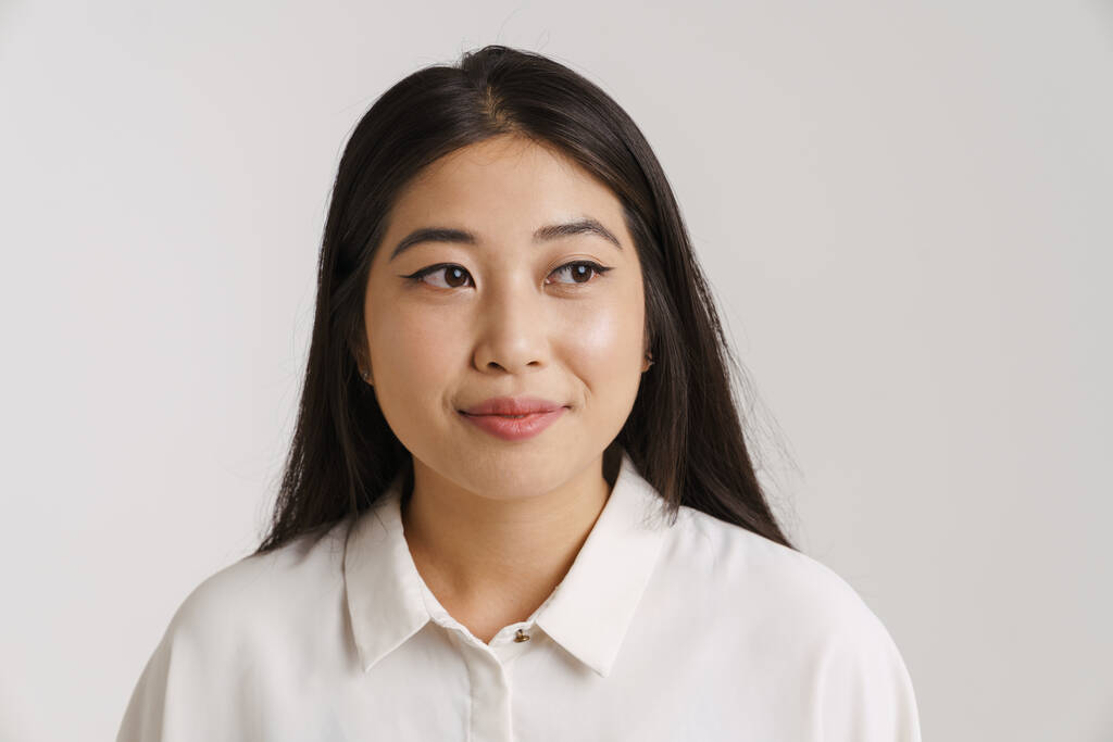 Молода азіатська жінка одягнена сорочка посміхається і виглядає ізольовано над білою стіною
 - Фото, зображення