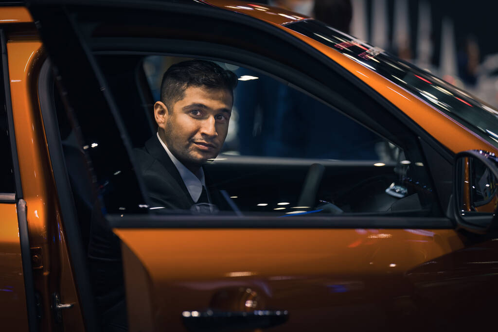Kaukasische zakenman in een auto in autoshow of showroom op zoek naar nieuwe auto om te kopen - Foto, afbeelding