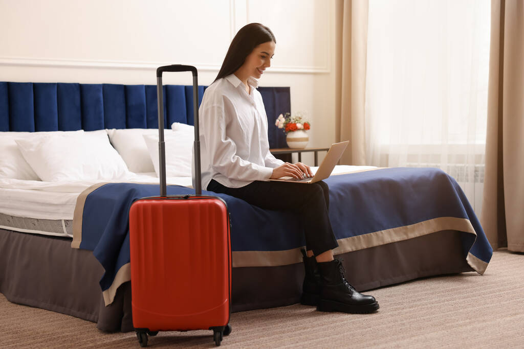 Krásná mladá obchodní žena pracující s notebookem na posteli v hotelovém pokoji - Fotografie, Obrázek