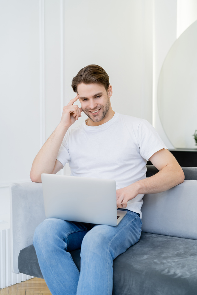 iloinen mies käyttää kannettavaa tietokonetta istuessaan sohvalla kotona - Valokuva, kuva