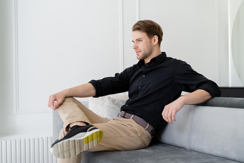uomo in camicia nera e pantaloni beige seduto sul divano in salotto - Foto, immagini