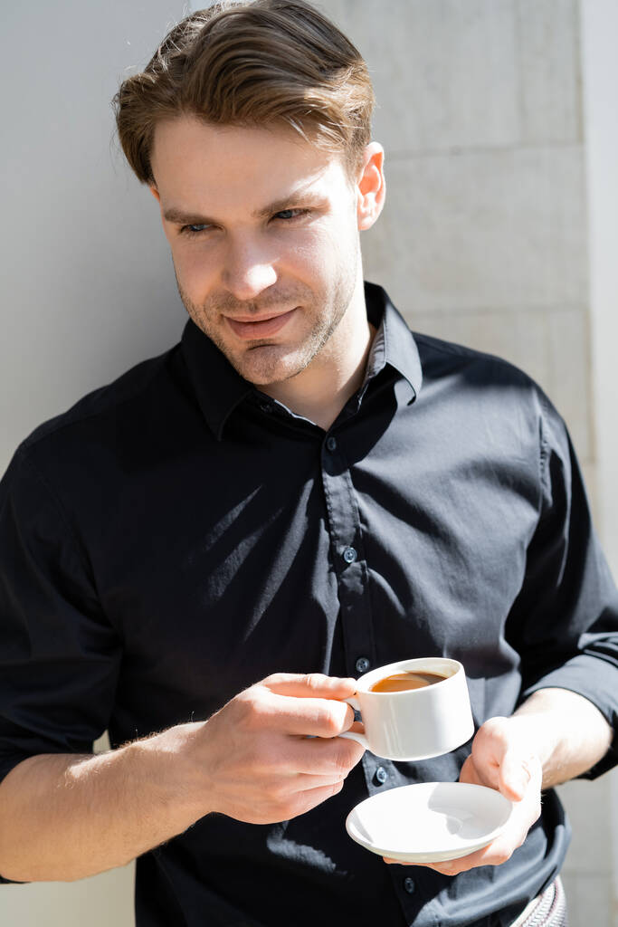 pozitív férfi fekete ingben kezében reggeli kávé árnyékban - Fotó, kép