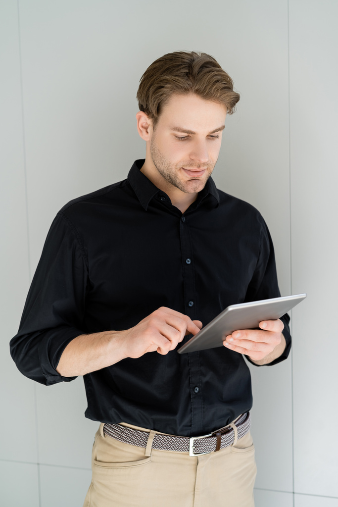 mies mustassa t-paidassa käyttäen digitaalista tablettia seistessään harmaan seinän lähellä - Valokuva, kuva