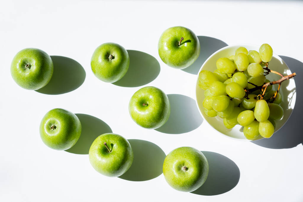 vista superior de manzanas cerca de uvas sabrosas en tazón sobre blanco - Foto, Imagen