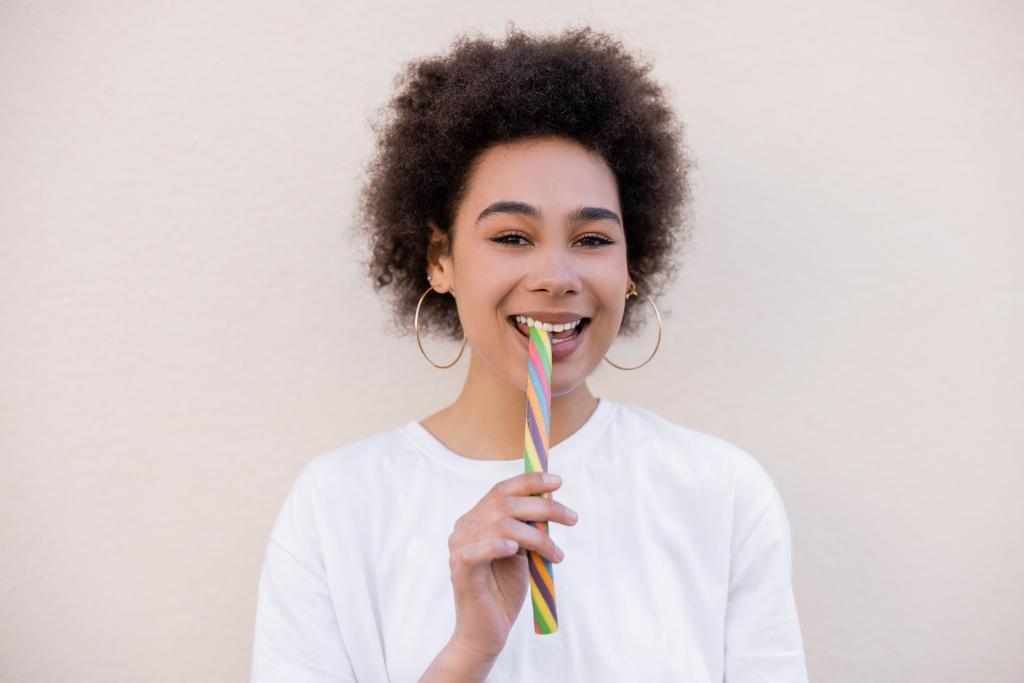 boldog afro-amerikai fiatal nő karika fülbevaló eszik zselés csík fehér - Fotó, kép