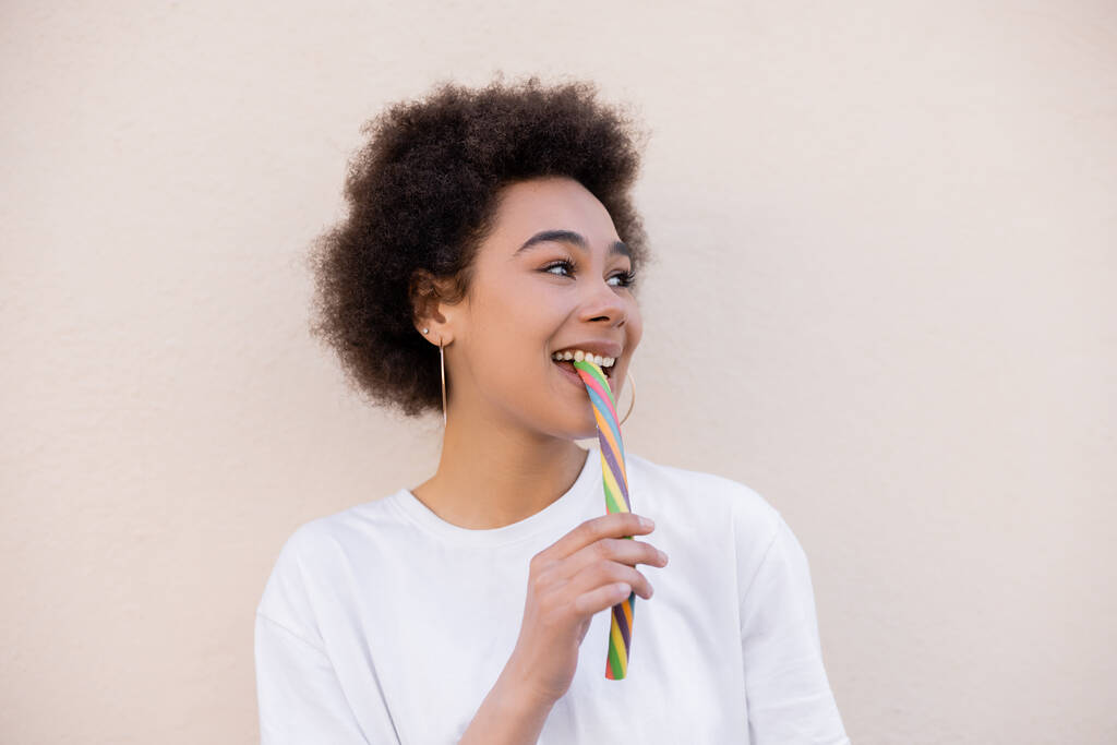 θετική αφροαμερικανή νεαρή γυναίκα τρώει καραμέλα ζελέ σε λευκό - Φωτογραφία, εικόνα