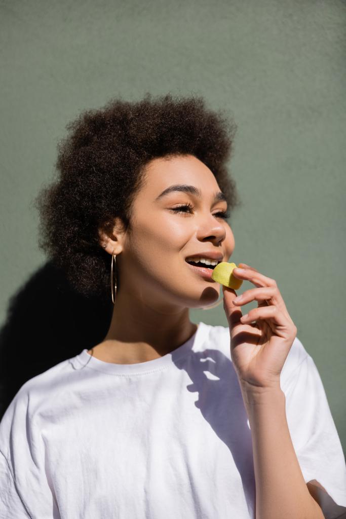 cheerful african american woman eating yellow candy  - Foto, Bild