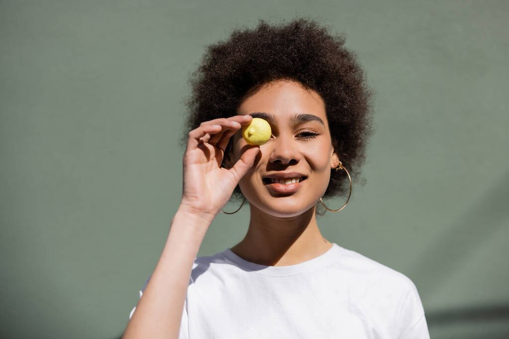 heureuse afro-américaine femme couvrant oeil avec des bonbons jaunes  - Photo, image