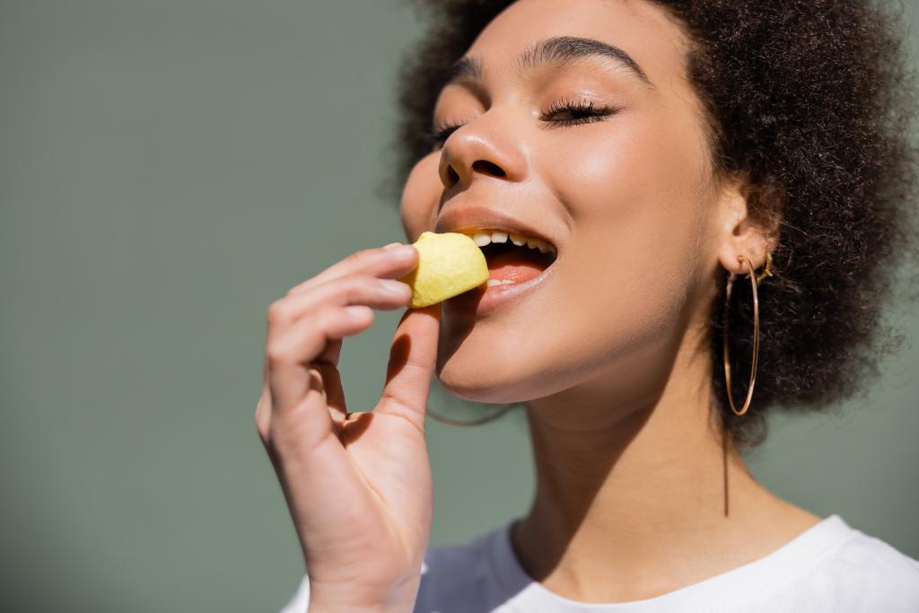 mujer afroamericana complacida comiendo caramelos amarillos  - Foto, Imagen