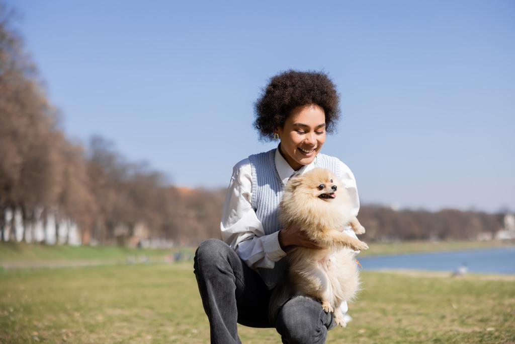 cheerful african american woman holding in arms pomeranian dog - Foto, imagen