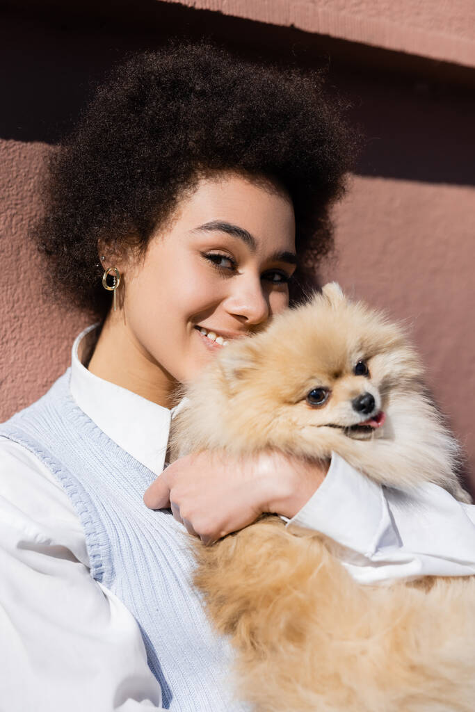 happy african american woman holding in arms pomeranian spitz and looking at camera - Foto, imagen
