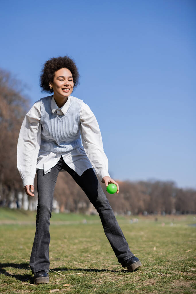 teljes hossza mosolygós afro-amerikai nő ing és mellény holding ball a parkban - Fotó, kép